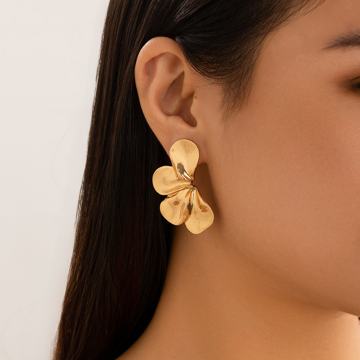 Gold flower-shaped earring worn by a person with a neutral background