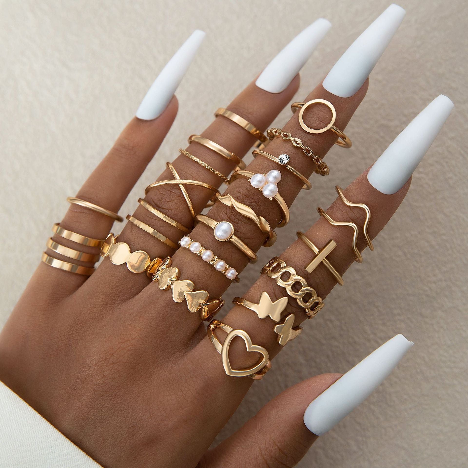 Hand wearing multiple gold rings with various designs on a neutral background