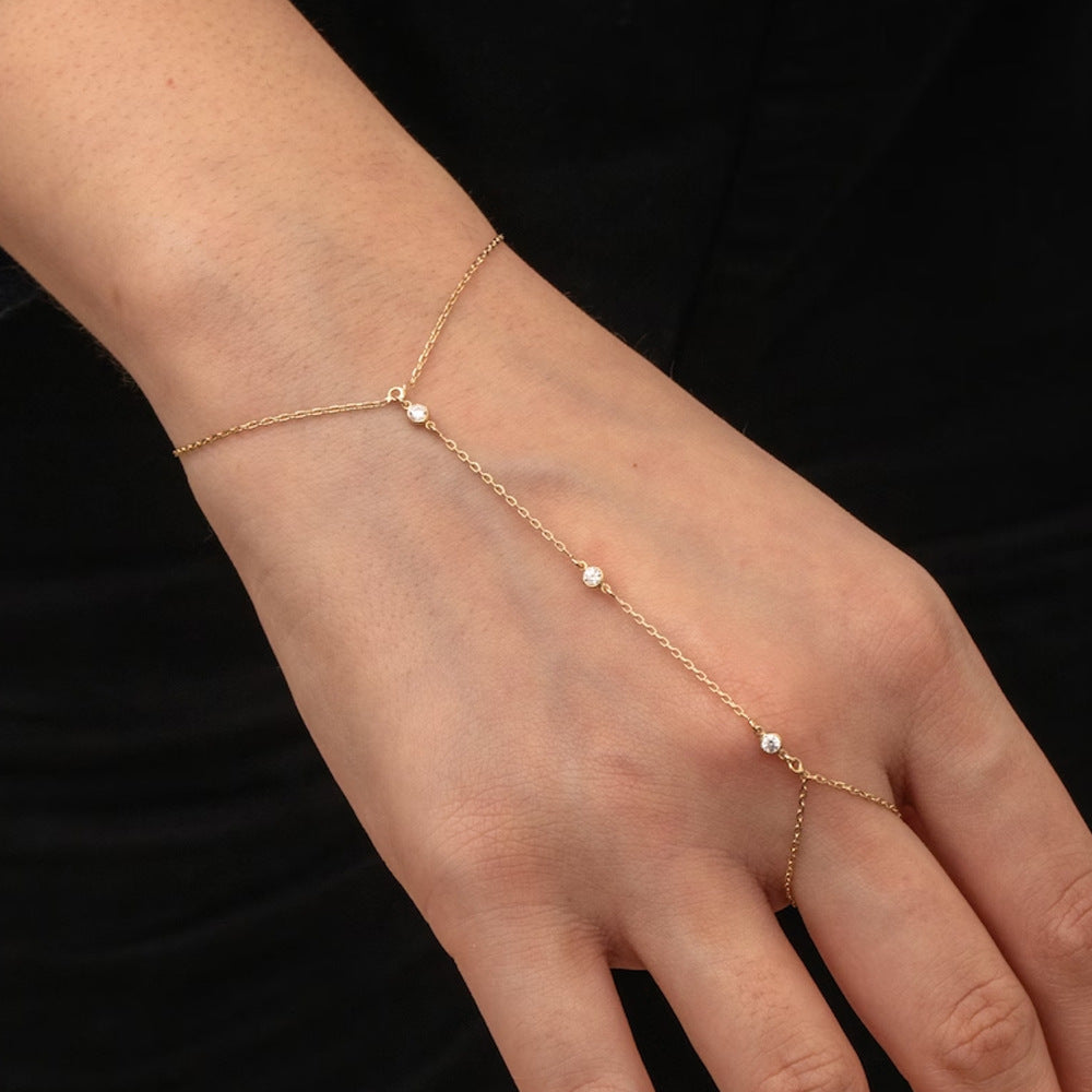 Rose gold hand chain on a hand against a black background
