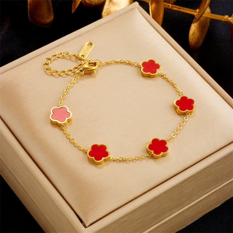 Gold bracelet with red flower-shaped charms on a beige jewelry box.