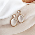 Pair of gold-framed white earrings on a soft fabric background