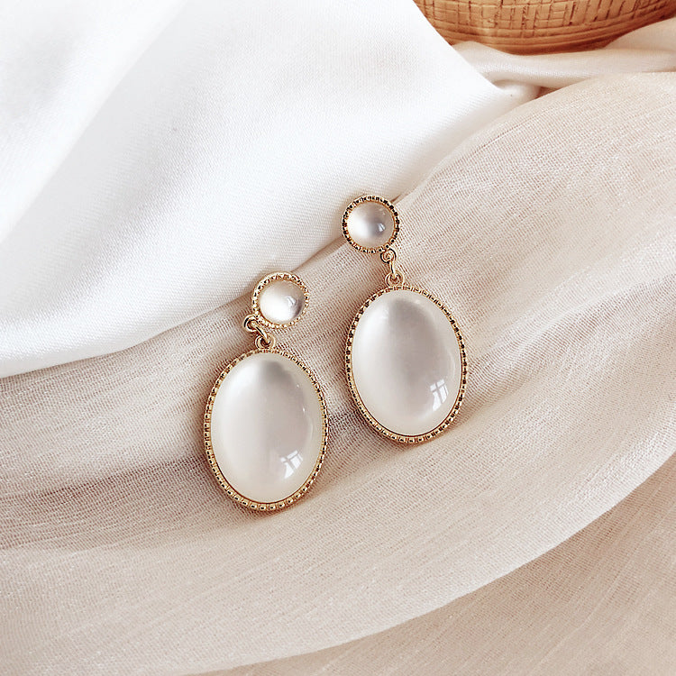 Pair of gold-framed white earrings on a soft fabric background