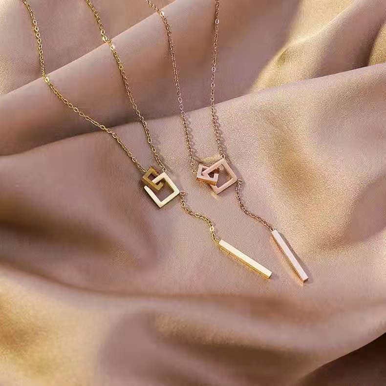 Three gold necklaces with geometric pendants on a hand.