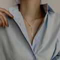 Necklace with square pendant worn by a person in a light blue shirt.
