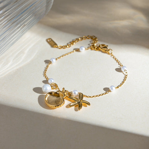 Gold bracelet with starfish and pearl charms on a beige surface