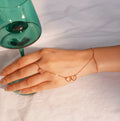Hand wearing a delicate bracelet with a green glass object in the background