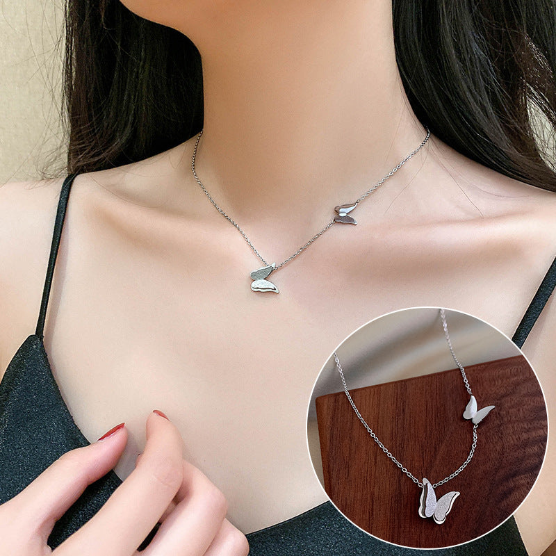 Silver butterfly necklace worn by a person, with an inset showing a close-up of the necklace on a wooden surface.