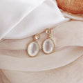 Pair of gold and white earrings on a soft fabric background