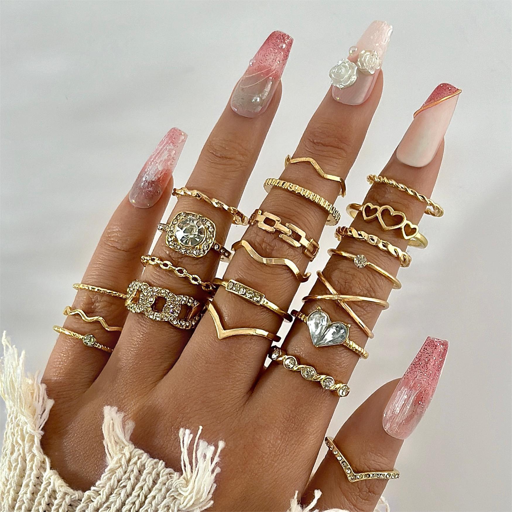 Hand wearing multiple gold rings with decorative nail art on a neutral background