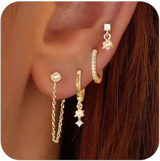 Gold earrings with gemstones worn on an ear against a neutral background