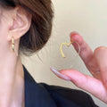 Gold heart-shaped earring held by a hand with a blurred background