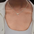 Gold bow-shaped necklace on a person wearing a light gray top.