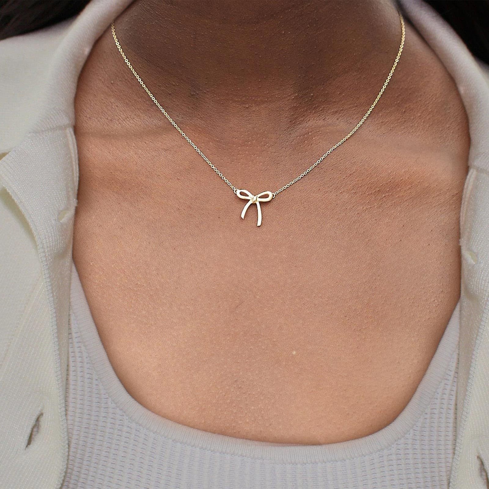 Gold bow-shaped necklace on a person wearing a light gray top.