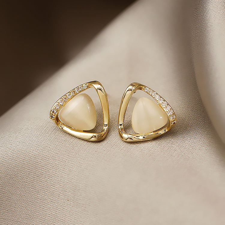 Gold earrings with white stones on a beige fabric background