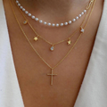 Layered gold and pearl necklaces on a person wearing a white top.