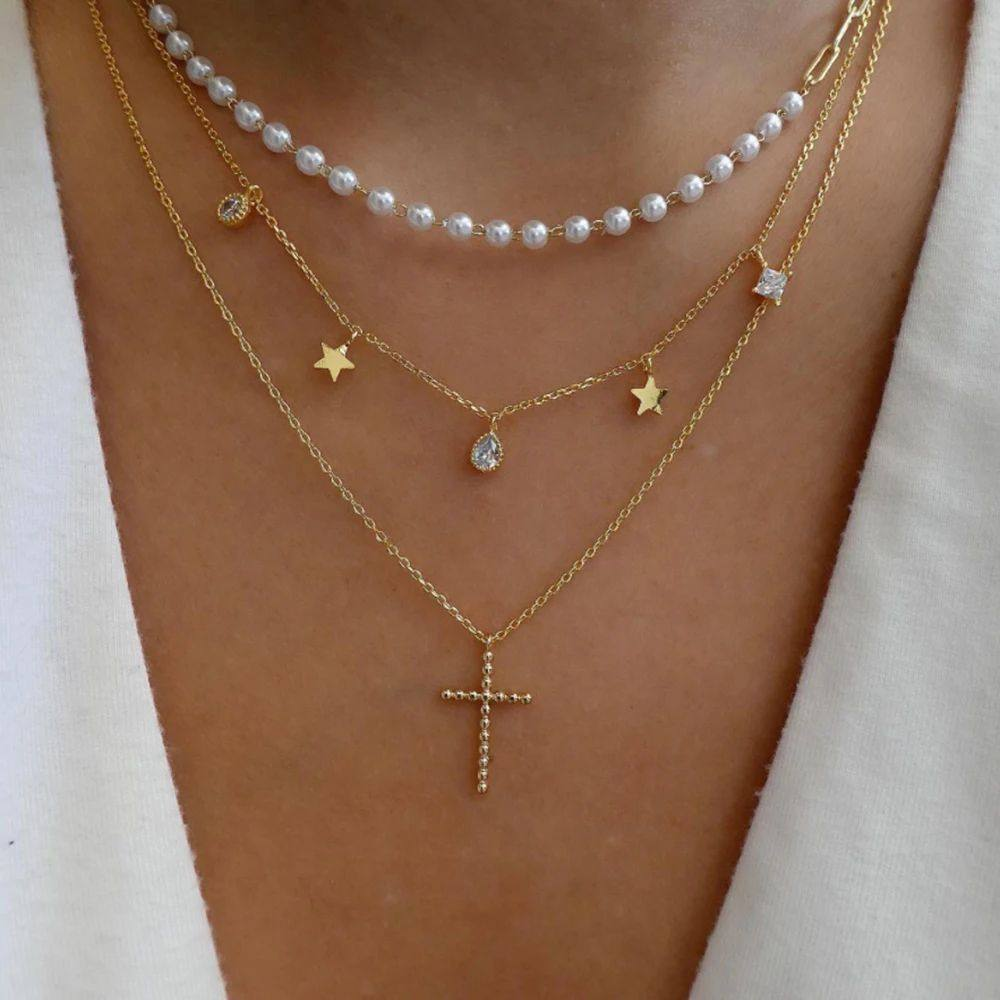 Layered gold and pearl necklaces on a person wearing a white top.
