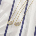 Two gold necklaces with druzy pendants on a white and blue striped fabric background