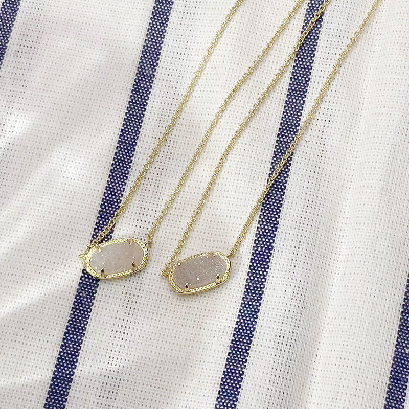 Two gold necklaces with druzy pendants on a white and blue striped fabric background