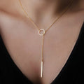 Gold necklace with a circular pendant and a vertical bar on a person wearing a black top.