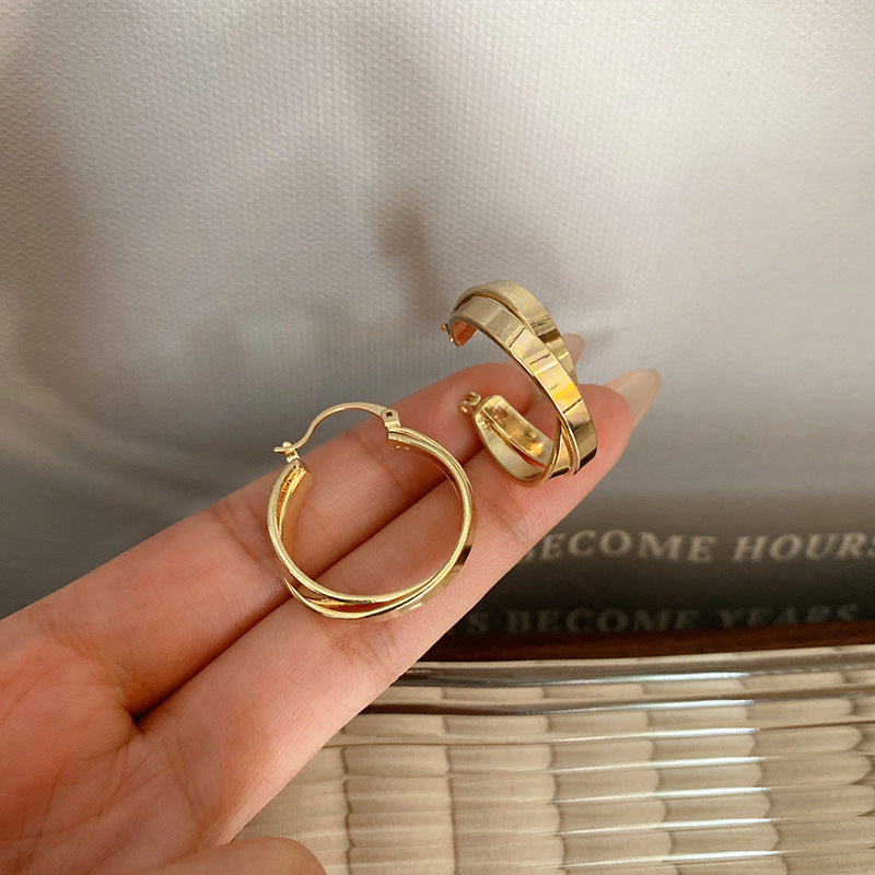 Gold hoop earrings held in a hand with a neutral background