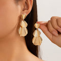 Gold earrings being worn by a person with a neutral background