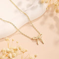 Gold bow-shaped necklace on a soft beige background with dried flowers.