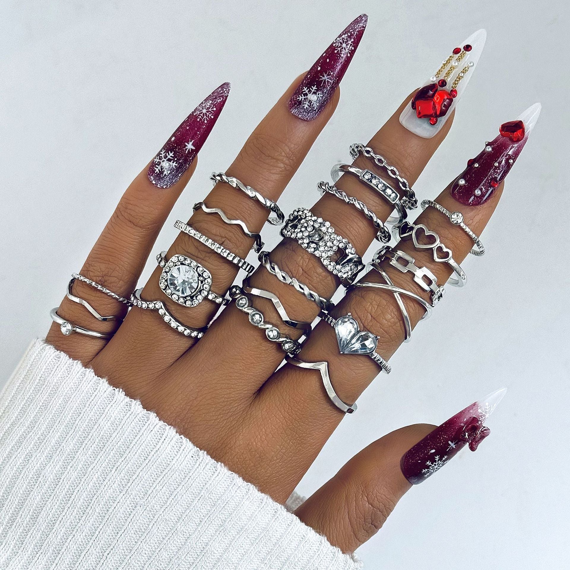 Hand wearing multiple silver rings with decorative nails on a light background