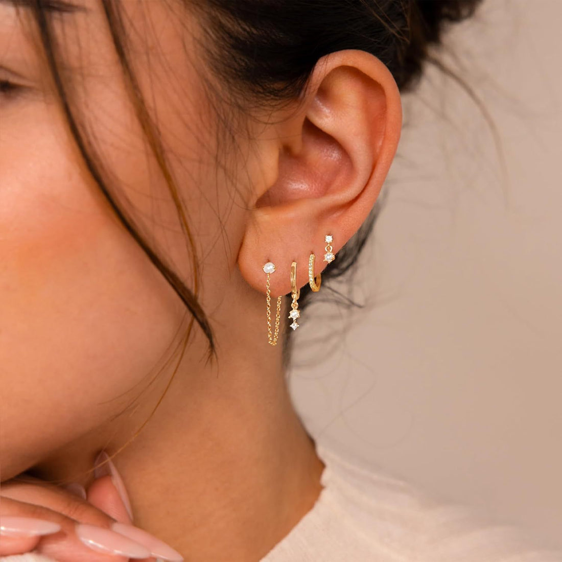 Close-up of a person wearing gold earrings with small stones.