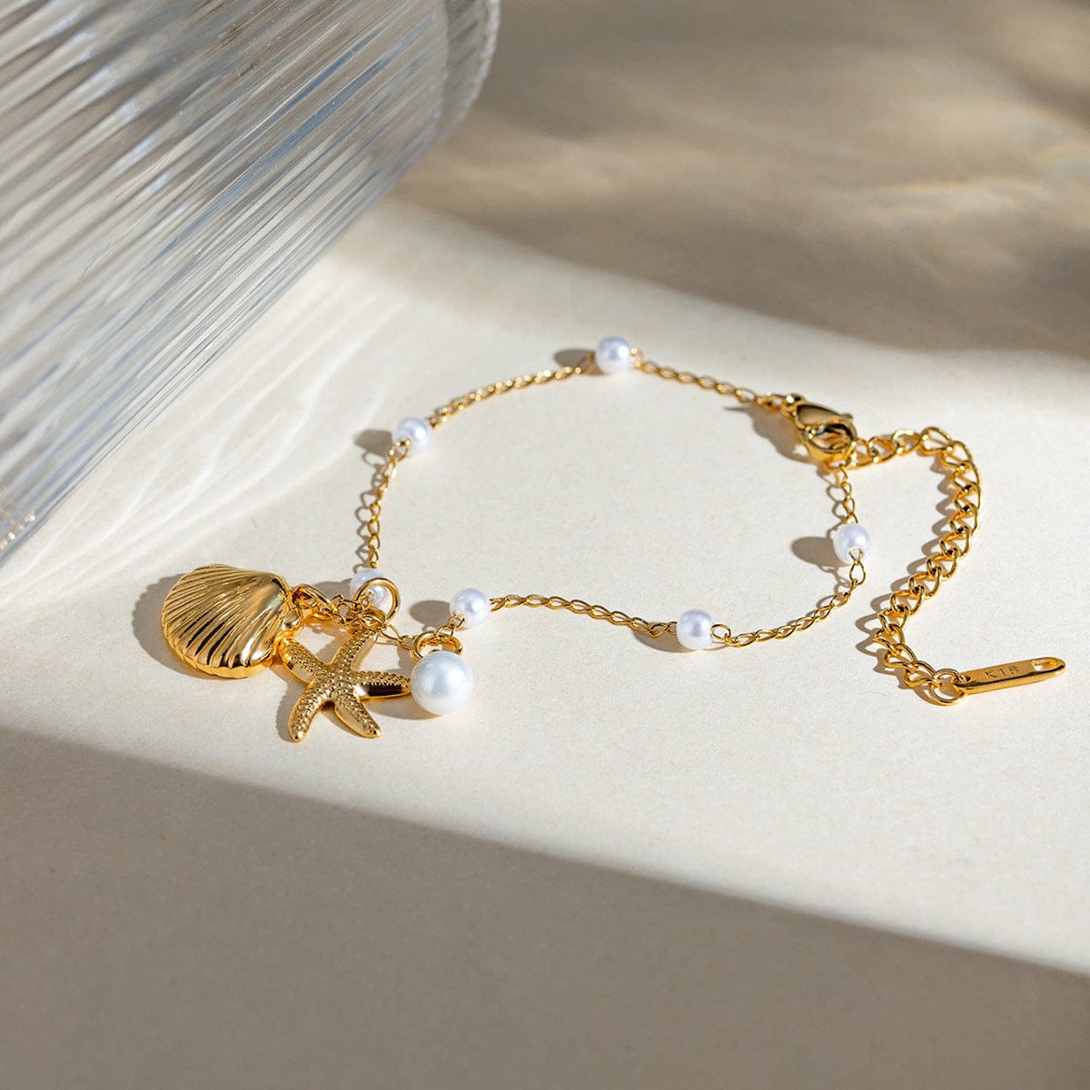 Gold bracelet with shell and starfish charms on a beige surface