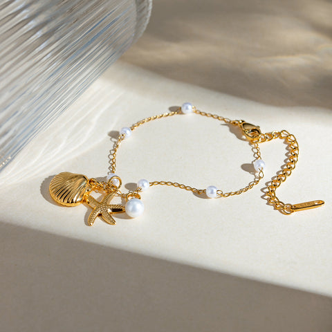 Gold bracelet with shell and starfish charms on a beige surface