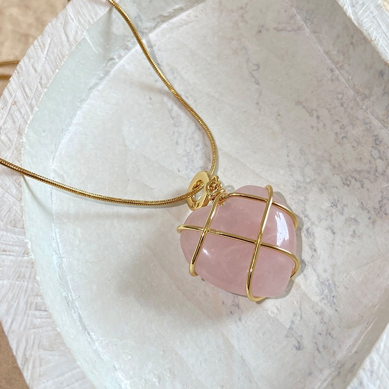 Pink stone pendant with gold wire wrapping on a marble surface