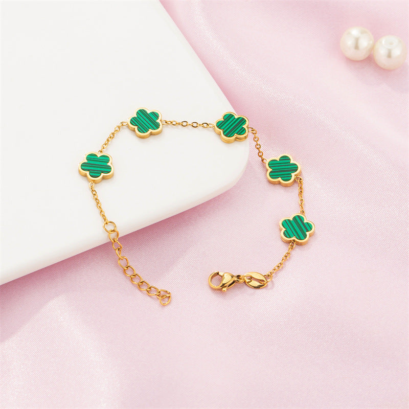Gold bracelet with green clover-shaped charms on a pink background