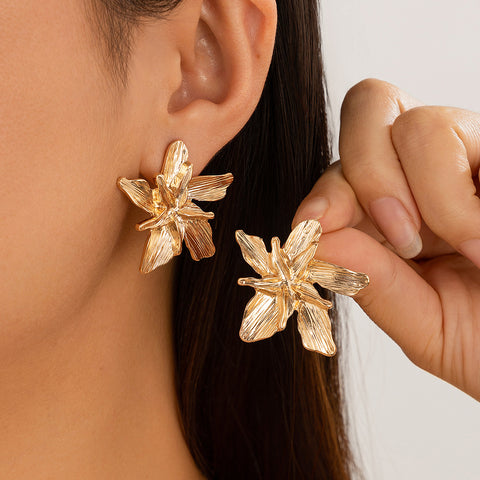 Gold floral earrings being worn and held by a person.