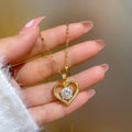 Gold heart-shaped necklace with a clear gemstone held by a hand against a blurred background