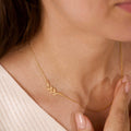 Gold necklace with leaf design worn by a person, close-up on neck and chest.