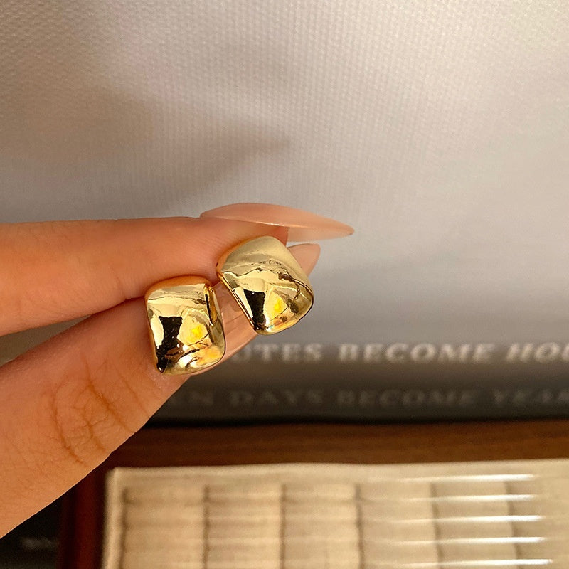 Gold hoop earrings held between fingers with a neutral background