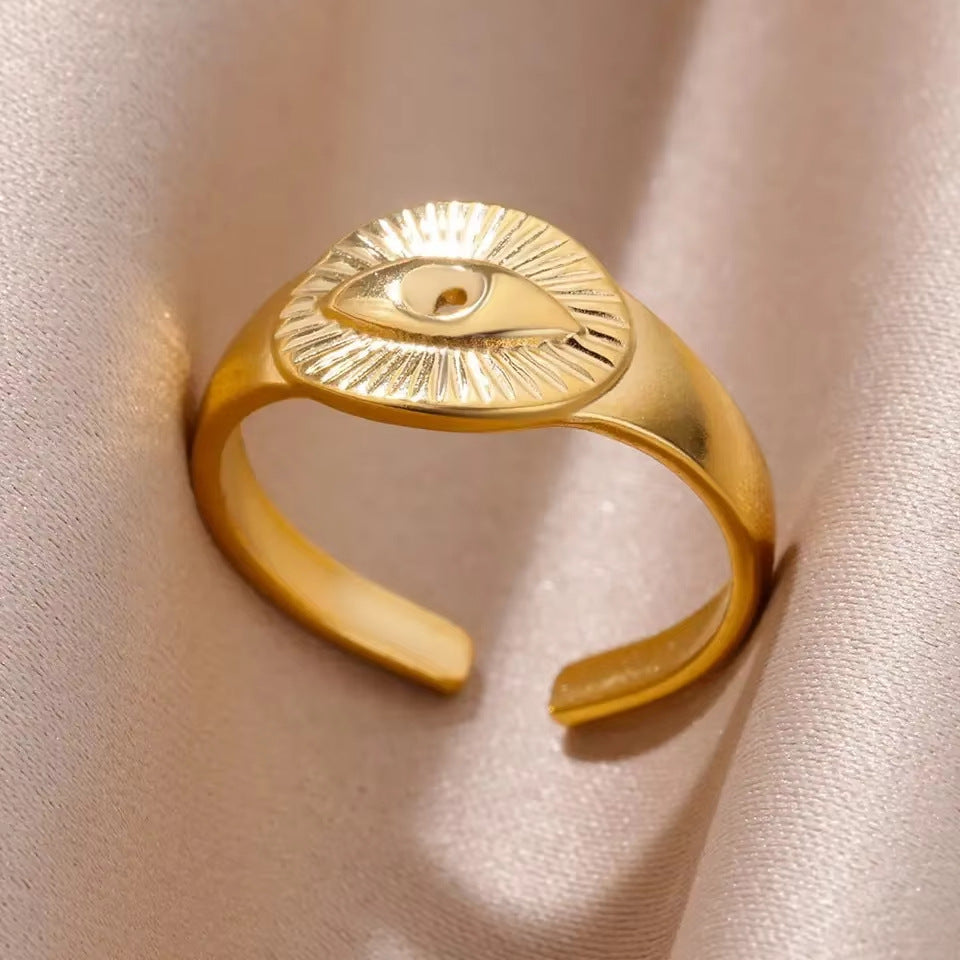 Gold ring with an eye design on a light pink fabric background