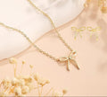 Gold bow-shaped necklace and earrings on a soft beige background with dried flowers.