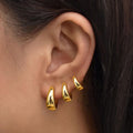 Close-up of an ear wearing gold hoop earrings with dark hair in the background