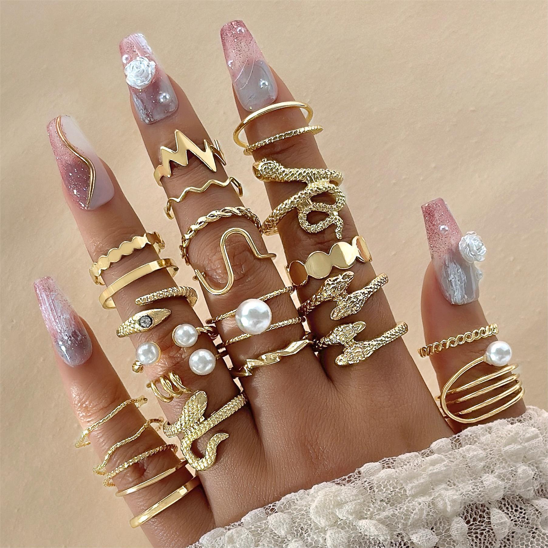 Hand wearing multiple gold rings with various designs on a beige background