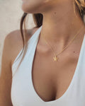 Gold necklace with a turtle pendant worn by a person in a white top.