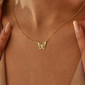 Gold butterfly necklace on a person's chest against a brown background