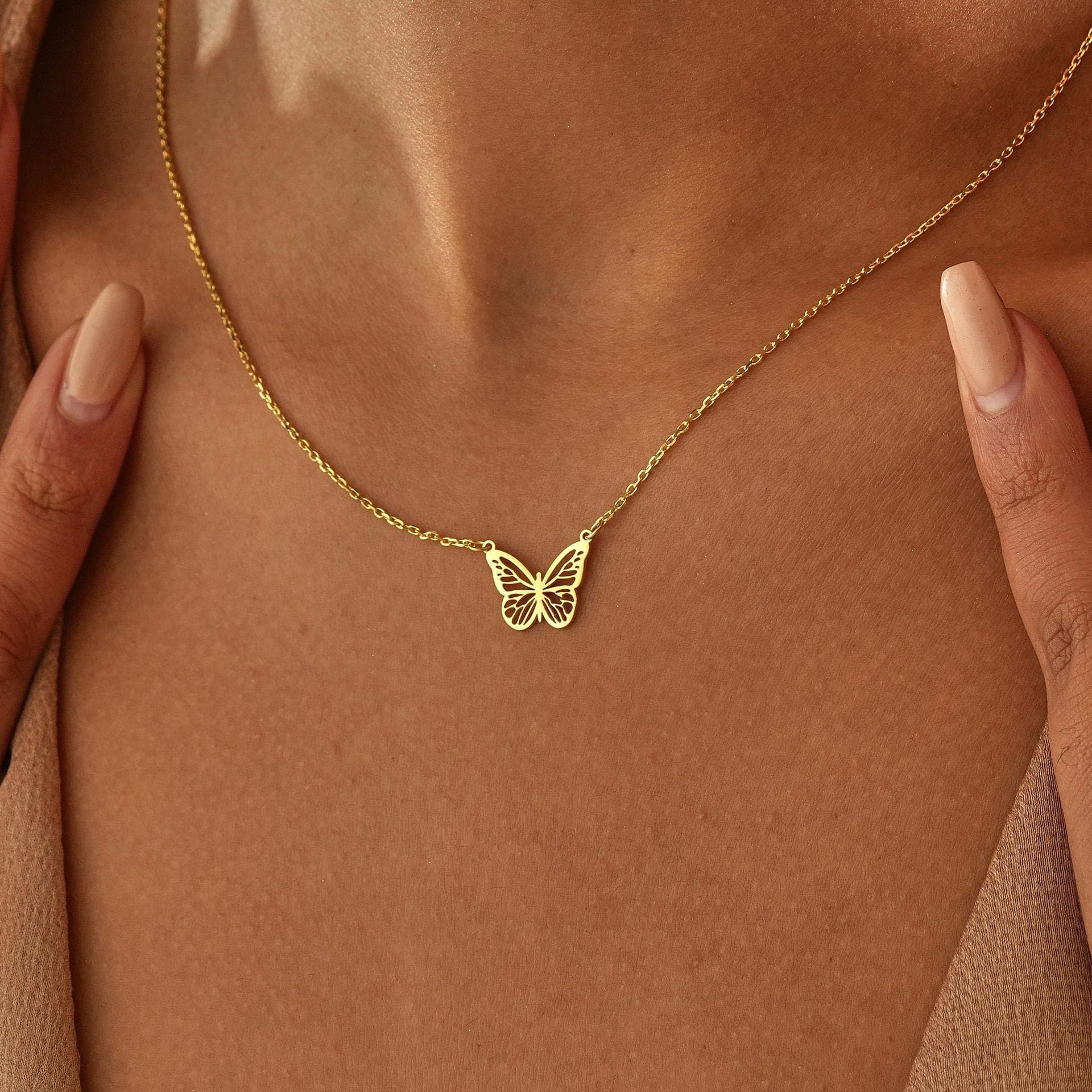 Gold butterfly necklace on a person's chest against a brown background