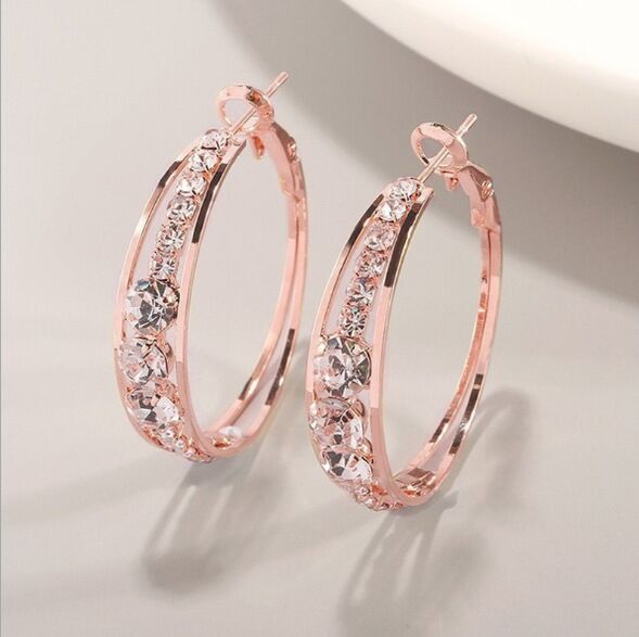 Rose gold hoop earrings with clear gemstones on a light gray background