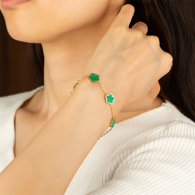 Close-up of a person wearing a gold bracelet with green clover charms.