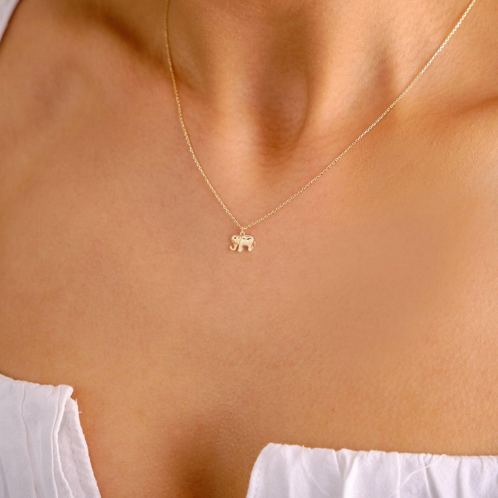 Gold necklace with an elephant pendant on a person wearing a white top.