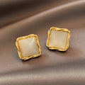 Gold square earrings with beige stones on a brown fabric background