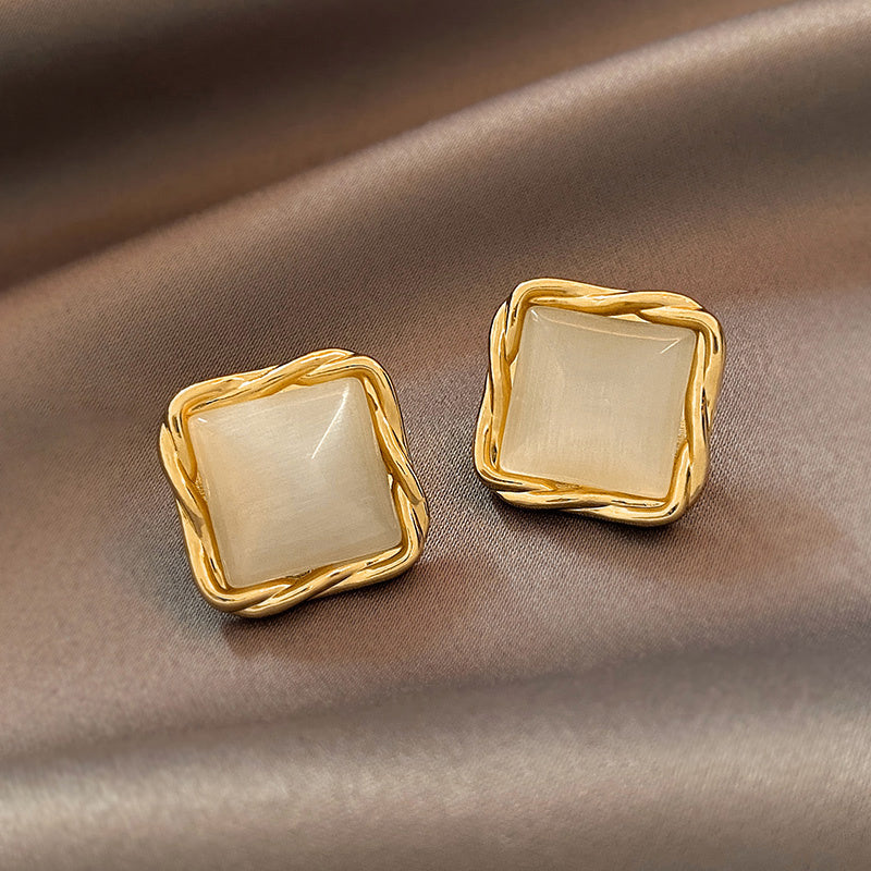 Gold square earrings with beige stones on a brown fabric background
