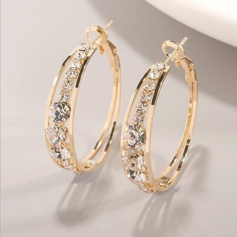 Gold hoop earrings with clear gemstones on a light gray background