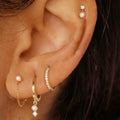 Close-up of an ear wearing gold hoop earrings with pearl-like stones.